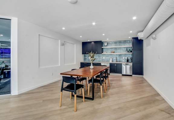 a dining area with a wooden table and chairs and a kitchen in the background