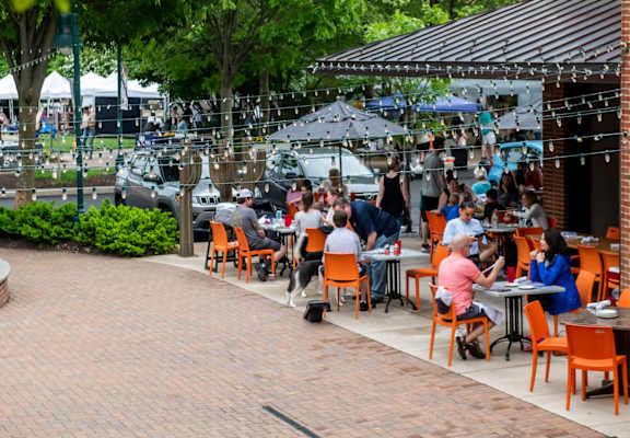 A group of people are sitting at tables under a canopy in a courtyard.