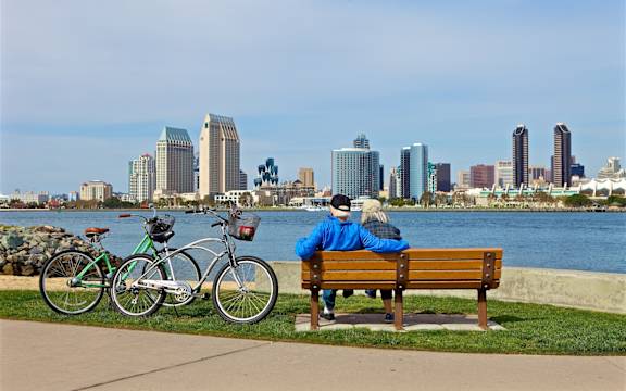 A couple is sitting on a bench by a body of water with bicycles parked nearby.