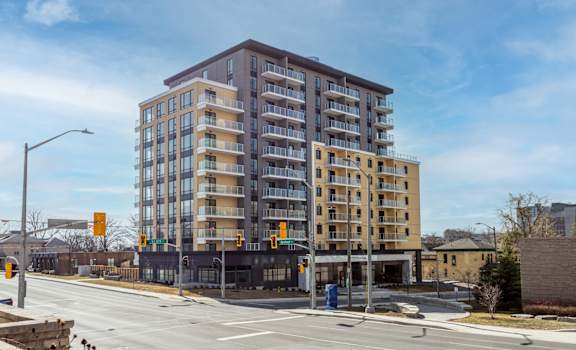 A large apartment building is situated on a street corner with a traffic light and a pedestrian crossing.