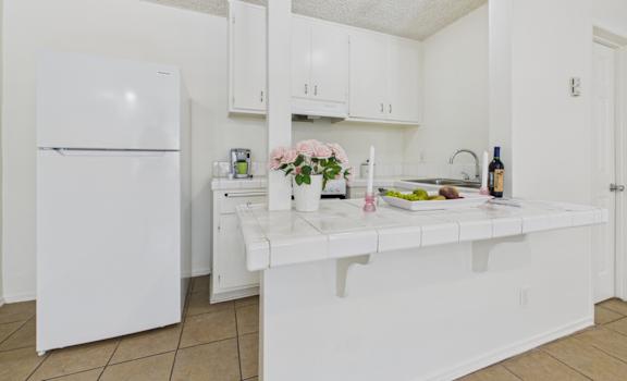 A white kitchen with a refrigerator, sink, and countertop.