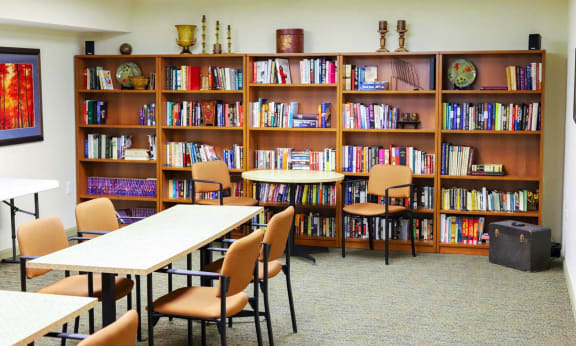 A room with a long bookshelf filled with books and a table with chairs in front of it.