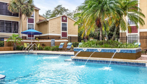 a swimming pool with trees and buildings in the background  at Hidden Palms Apartment Homes, Tampa, Florida