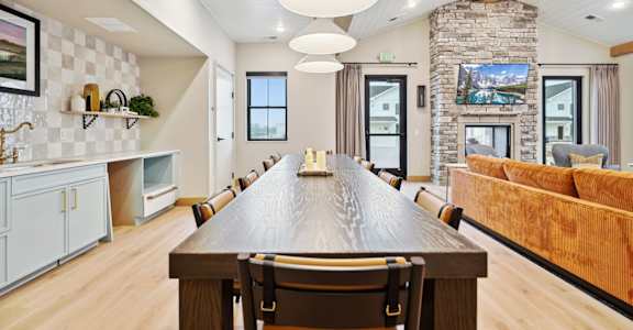 A long wooden table is in the middle of a room with a stone pillar and a couch.