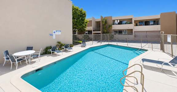 A swimming pool with a white fence and chairs around it.