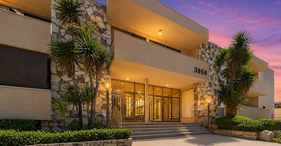 A modern building with a stone wall and palm trees in front.