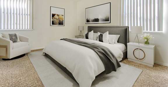 A bedroom with a large bed, a white armchair, and two framed pictures on the wall.