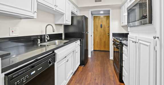 a kitchen with white cabinets and black appliances and a door to a hallway