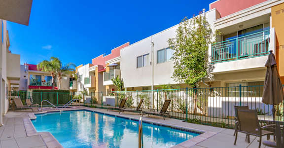 A pool surrounded by a white fence and chairs.