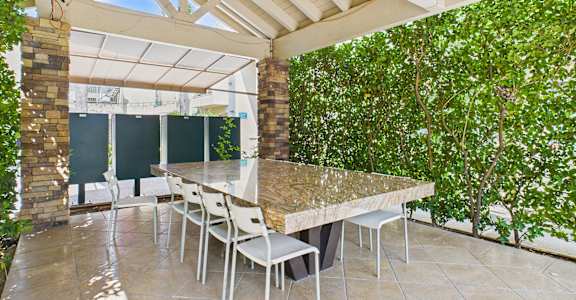 A patio with a table and chairs is surrounded by greenery.