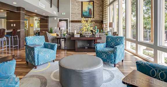 a lobby with blue chairs and a table and large windows at Whisper Lake Apartments, Winter Park, 32792