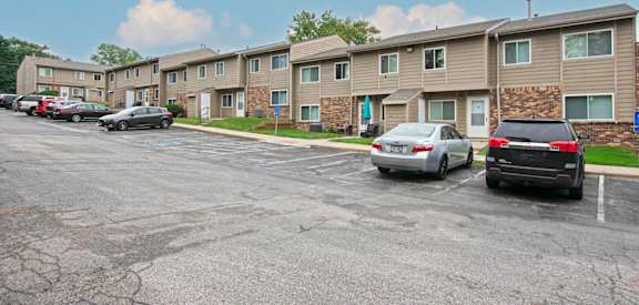 A parking lot in front of apartment buildings with cars parked.