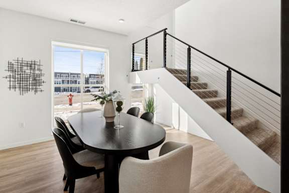 A black table with four chairs is in a room with a staircase.