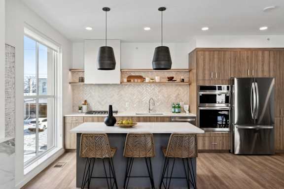 A modern kitchen with a white countertop and wooden chairs.