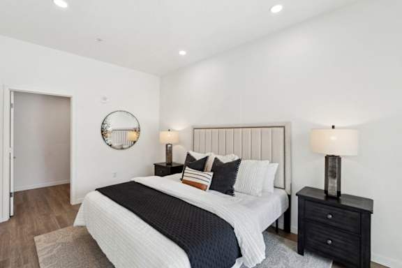 A bedroom with a large bed, a round mirror, and a nightstand with a lamp.