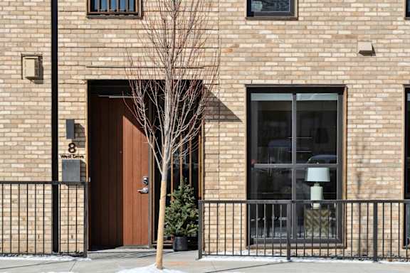 A brown door with a window above it and a tree in front of it.