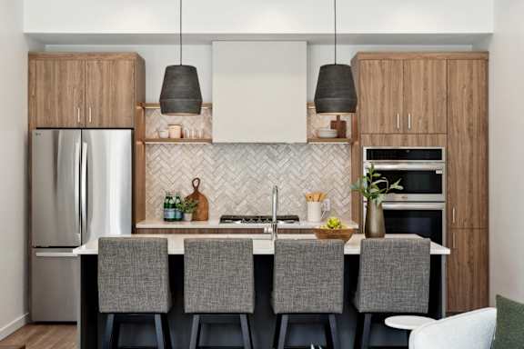 A modern kitchen with a white countertop and grey chairs.