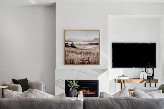 A living room with a grey couch, a fireplace, and a painting on the wall.