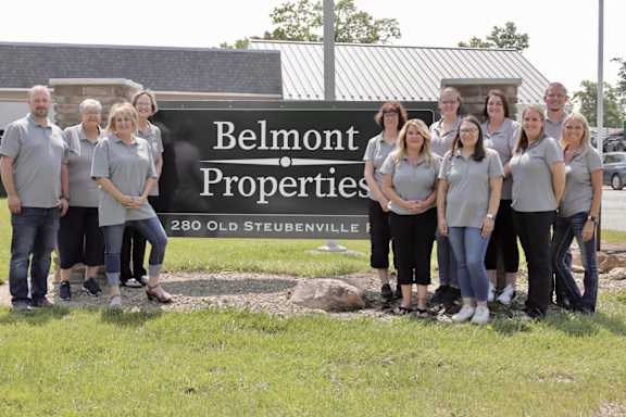 A group of people in matching shirts stand in front of a sign for Belmont Properties.