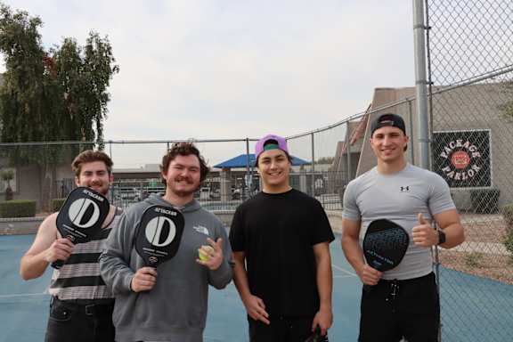 Four men are standing on a tennis court holding tennis rackets.