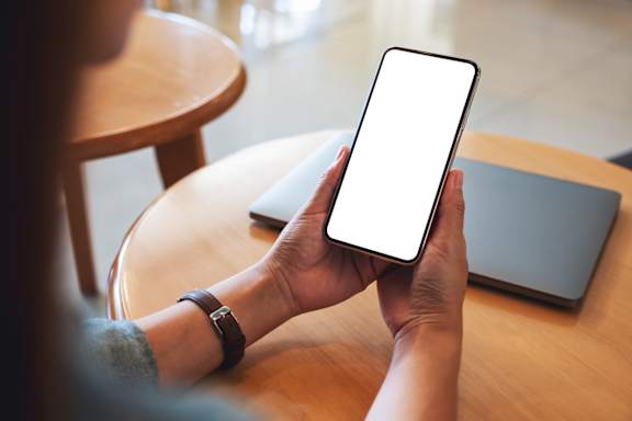 A person holding a smartphone with a white screen in a room.