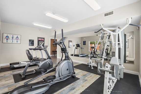 A gym with a variety of equipment including treadmills, elliptical machines, and weight machines.