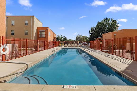 A swimming pool surrounded by orange fencing and buildings.