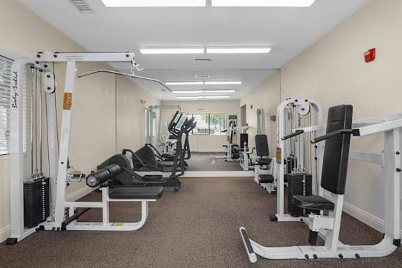 A gym with a variety of equipment including a weight bench, a leg press machine, and a cable machine.