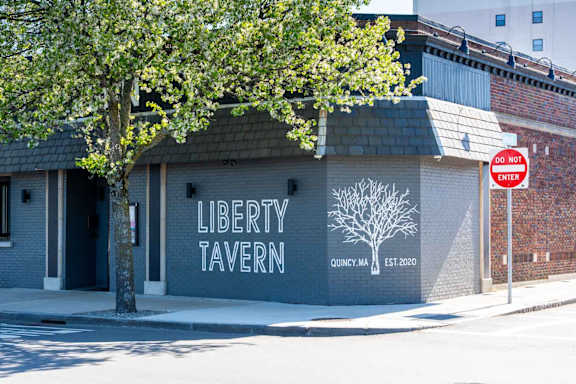 A white tree stands in front of a brick building with a sign that says "Liberty Tavern".