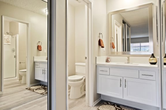 Single vanity area with white quartz counter tops, white cabinet, mirrored closet door and bathroom on the left