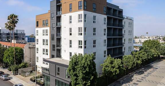 A modern apartment building with a parking lot in front at Skylar At Sunset Apartments, Los Angeles, CA