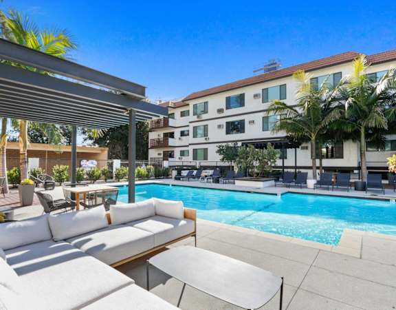 a swimming pool with a couch and tables in front of a building