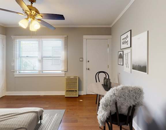 A room with a bed, a chair, a fan, and pictures on the wall.