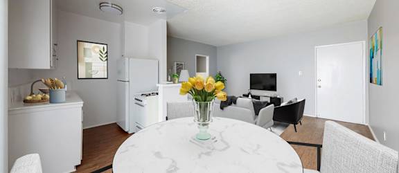 A white marble table with a vase of yellow flowers is in the middle of a modern kitchen and dining room.