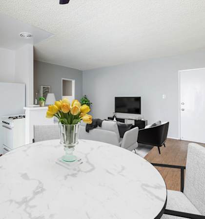 A white marble table with a vase of yellow flowers is in the middle of a modern kitchen and dining room.