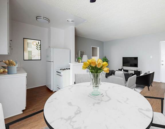 A white marble table with a vase of yellow flowers is in the middle of a modern kitchen and dining room.