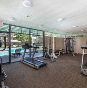 a large fitness room with cardio equipment and a pool in the background at Clair Del Gardens, Long Beach, 90807