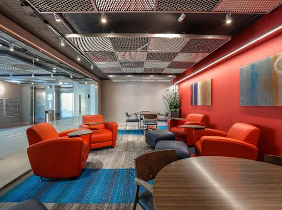 A modern office space with orange chairs and a wooden table at The Plaza Apartments, Los Angeles, CA