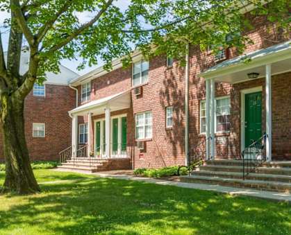 a brick building with green doors and a tree in front of it at Nottingham Manor Apartments, Montvale, New Jersey