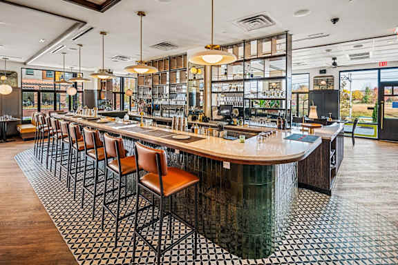 A long wooden bar with leather chairs and a black and white checkered floor.