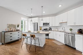 a kitchen with white cabinets and a white island with two chairs