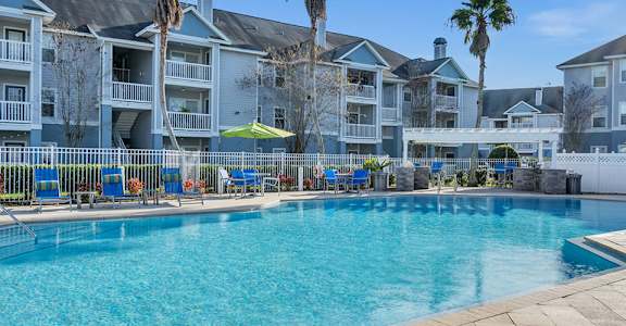 A large swimming pool surrounded by a white fence and blue lounge chairs.