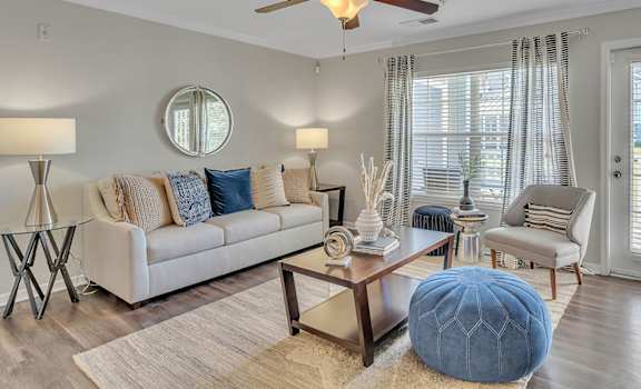 A living room with a white couch, a round mirror, and a ceiling fan.