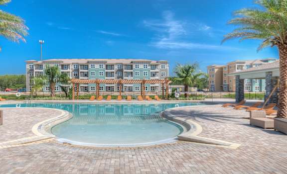 A large swimming pool surrounded by palm trees and apartment buildings.