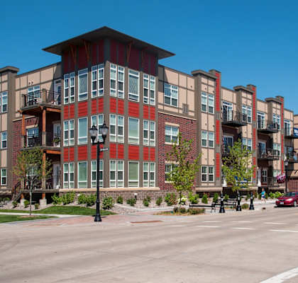 A street view of a multi-story building with a red car driving on the road.