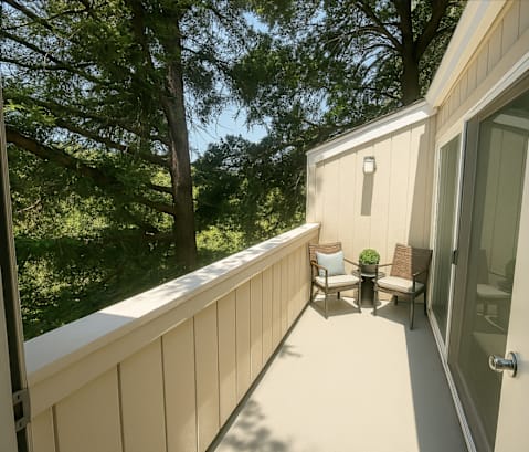 A balcony with a chair and a table is surrounded by trees.