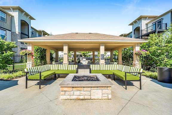 A gazebo with a fire pit in the middle of a courtyard surrounded by benches.