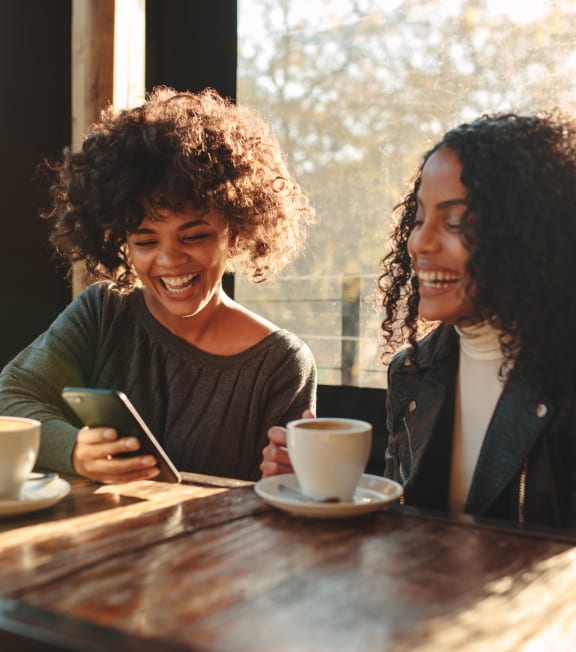 Women Sitting at Table Having Coffee and Smiling while Looking at Phone