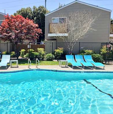 A swimming pool with blue water and lounge chairs in front of a building. at Stony Creek Apartments, Santa Rosa, 95401