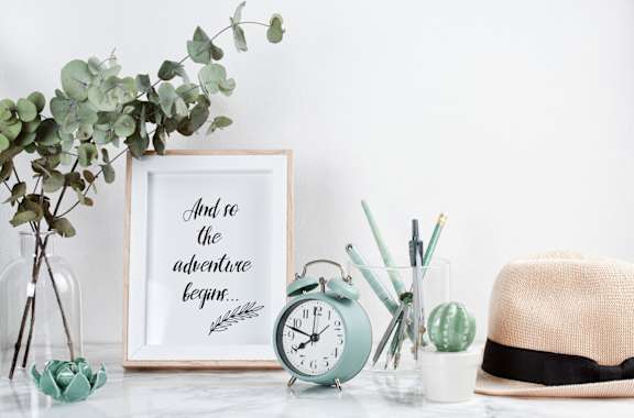 a desk with a clock and a frame with the quote and be the adventure again